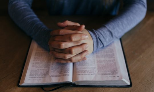 Hands pray on bible