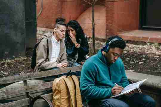 multiethnic-friends-gossiping-behind-attentive-classmate